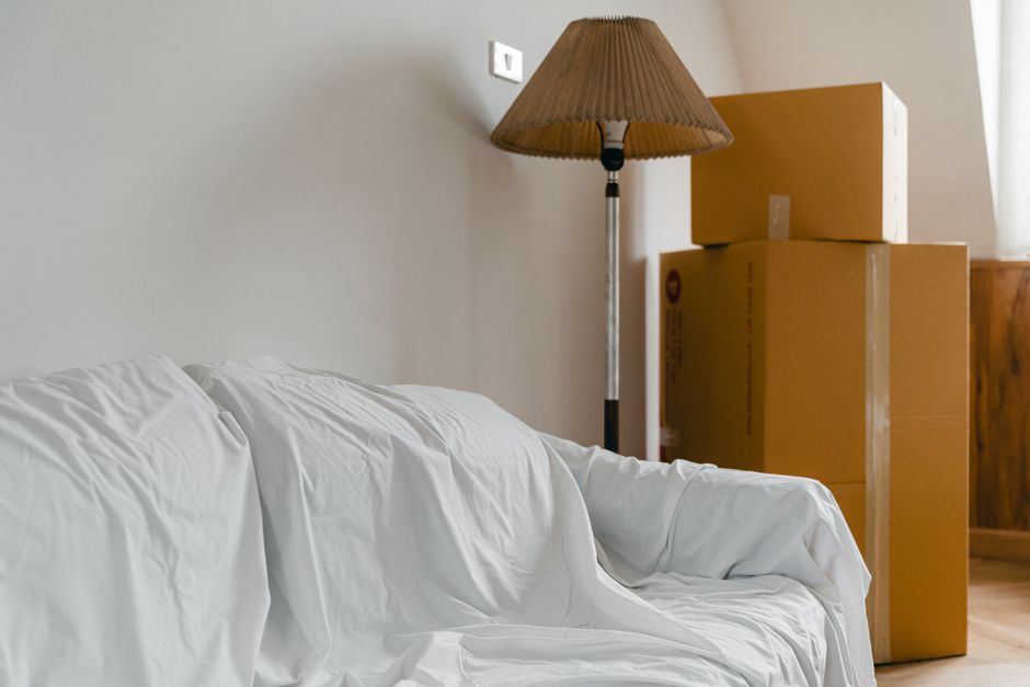 A sofa under a sheet beside large cardboard boxes