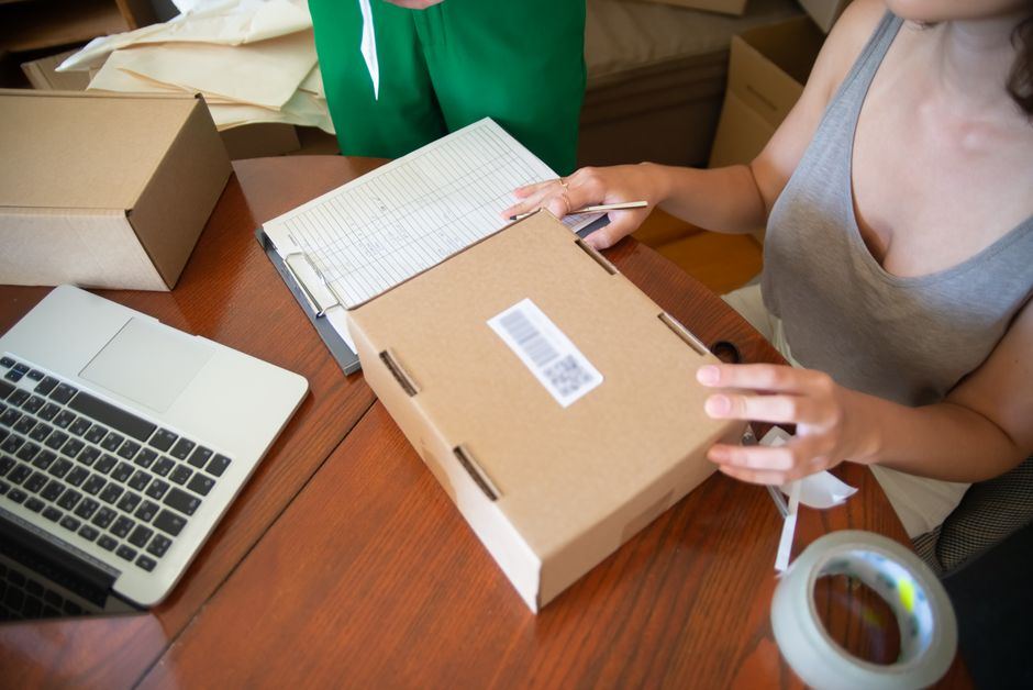A person taping a box shut beside a laptop