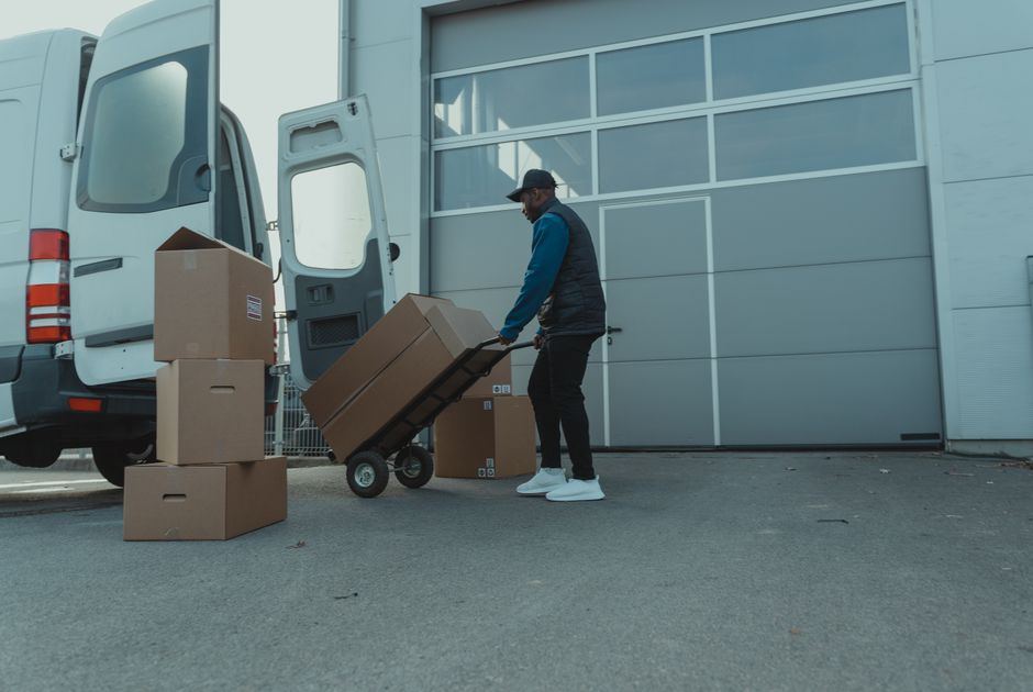 A worker unloading boxes from a van with a hand truck